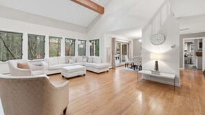 A spacious living room with a large sectional sofa, a white armchair, and a dining area with a table and chairs.
