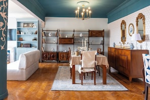 A dining area with a wooden table, chairs, and a chandelier. There is a bookshelf and a cabinet with decorative items. - Zamalek suuny khan (Cairo Governorate)