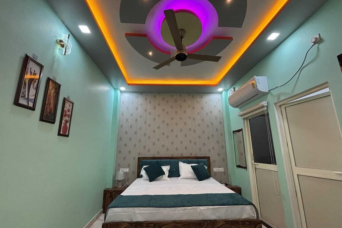 A bedroom with a bed, ceiling fan, wall-mounted air conditioner, and framed pictures on the wall.