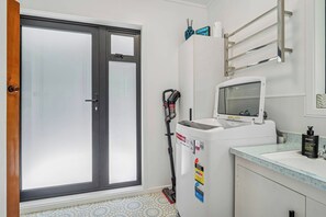 A bathroom with a glass door, a hand dryer, a sink, and a mirror. - Inn Manahi - Lake Views, Cosy Retreat for 2 (Rotorua)