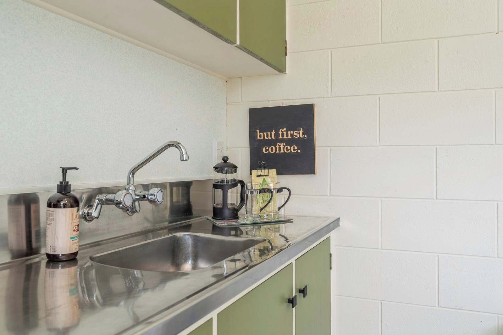 A kitchen with a stainless steel sink, a coffee maker, and a bottle of hand soap.