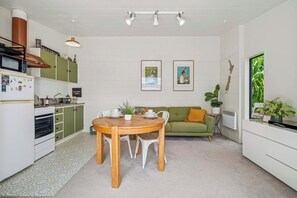 Une cuisine moderne avec un coin repas, comprenant une table et des chaises en bois, un canapé vert et une grande fenêtre donnant sur un paysage verdoyant.