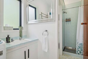 A bathroom with a mirror, sink, and shower. There is a towel hanging on the wall and a plant on the counter. - Inn Manahi - Lake Views, Cosy Retreat for 2 (Rotorua)