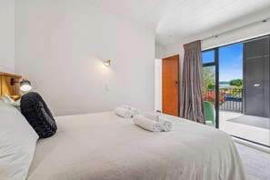 A modern hotel room with a large bed, a nightstand, a lamp, and a view of the outdoors through a sliding glass door. - Inn Manahi - Lake Views, Cosy Retreat for 2 (Rotorua)