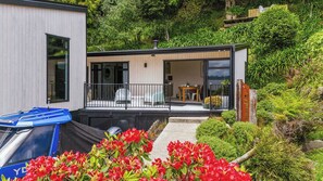 A modern house with a covered outdoor area, a car, and lush greenery. - Inn Manahi - Lake Views, Cosy Retreat for 2 (Rotorua)