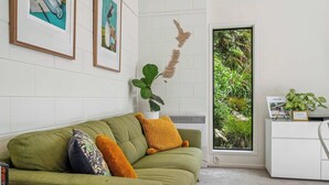 Ein grünes Sofa mit vielen Kissen, einer Blumentopf-Pflanze und gerahmten Kunstwerken an einer weißen Ziegelwand.