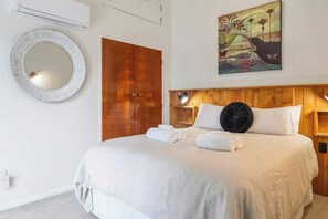 Une chambre d’hôtel avec un grand lit, une tête de lit en bois, un miroir rond, une armoire et un tableau accroché au mur.