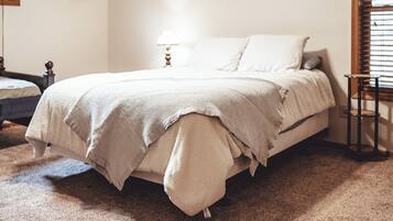 A neatly made bed with a white comforter and pillows, a bedside table with a lamp, and a small wooden stool.
