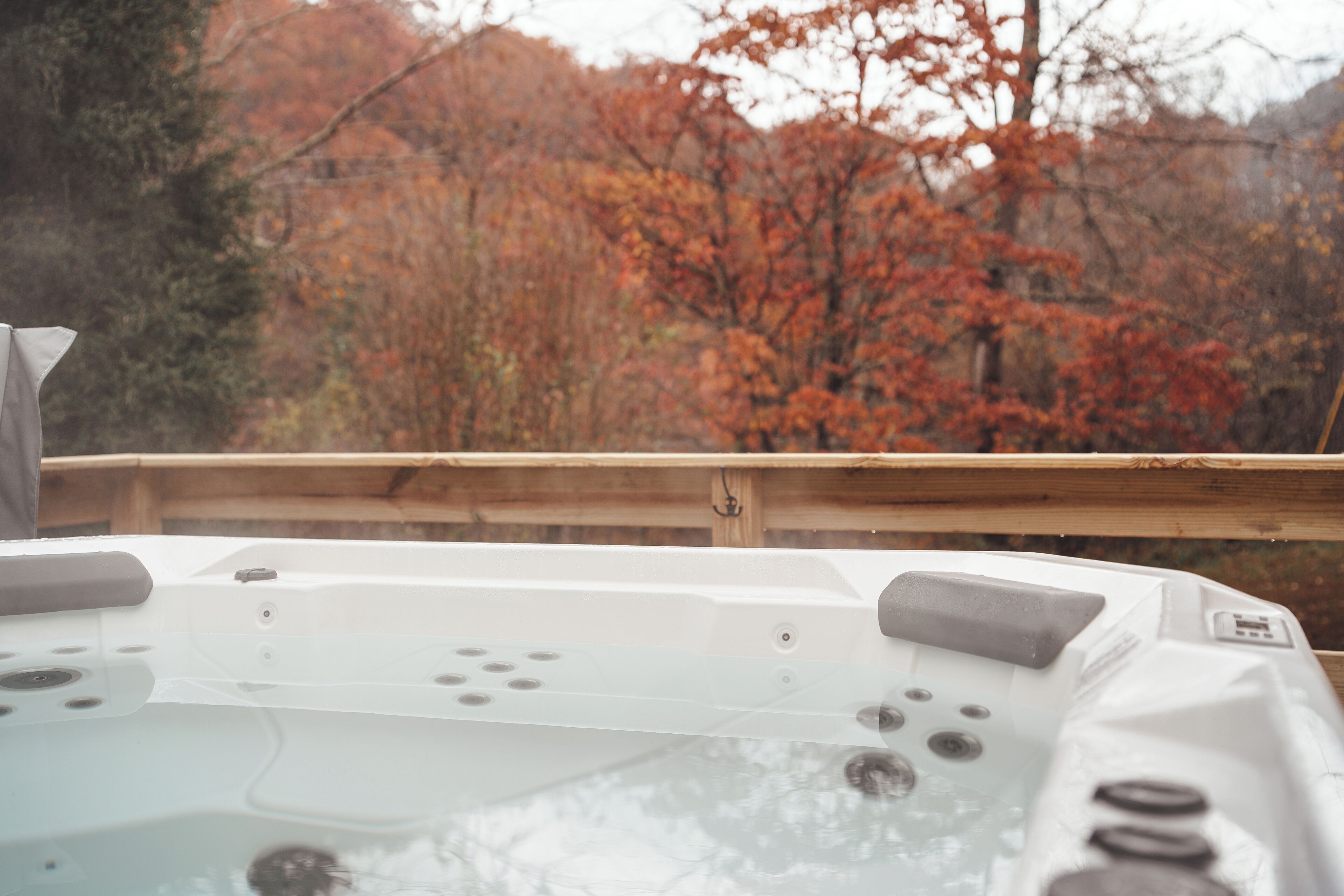A hot tub with a wooden deck and a view of autumn trees.