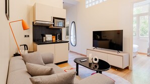 Moderni olohuone, jossa on sohva, sohvapöytä, televisio sekä keittiöalue, jossa on kaappeja ja mikroaaltouuni.