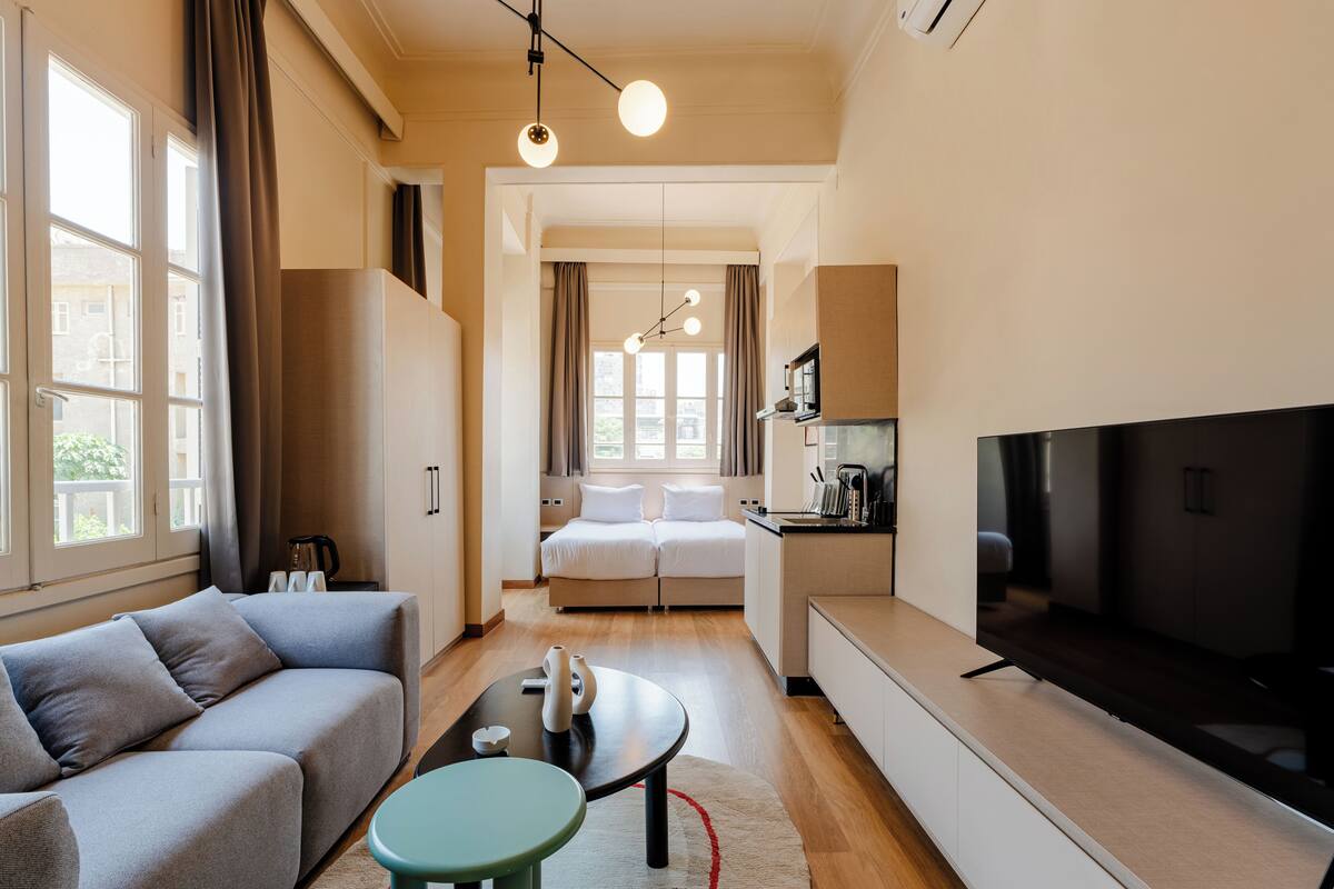 Una habitación de hotel moderna con sofá, una mesa de comedor, televisor y kitchenette.