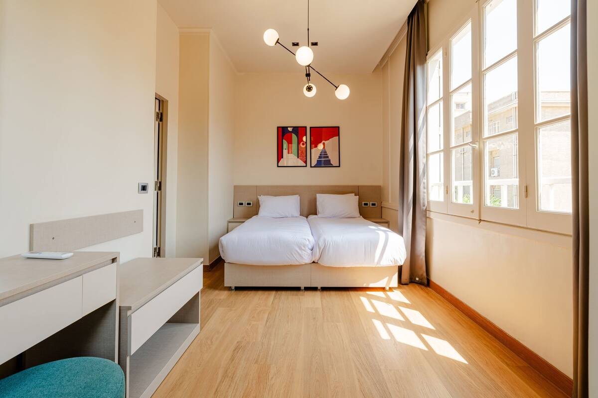 Una habitación de hotel moderna con una cama, mesitas de noche, un escritorio y una ventana con cortinas.