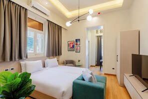 A hotel room with a bed, a green sofa, a TV, and a window with curtains. - Brassbell Zamalek High ceiling studios (Cairo)