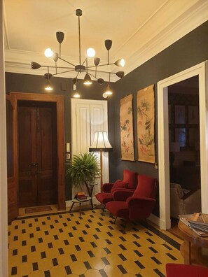 A room with a geometric patterned floor, a red armchair, a potted plant, and a chandelier with multiple lights. - Decopetit [The House of Timeless Charme freeWI-FI] (Torino)