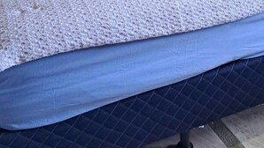 Une pièce aux murs lambrés, avec un lit, des oreillers et une petite étagère sur laquelle sont posés divers objets.
