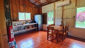 Une cuisine compacte avec un intérieur en bois, un réfrigérateur, une table à manger avec des chaises et une fenêtre donnant sur un espace verdoyant.