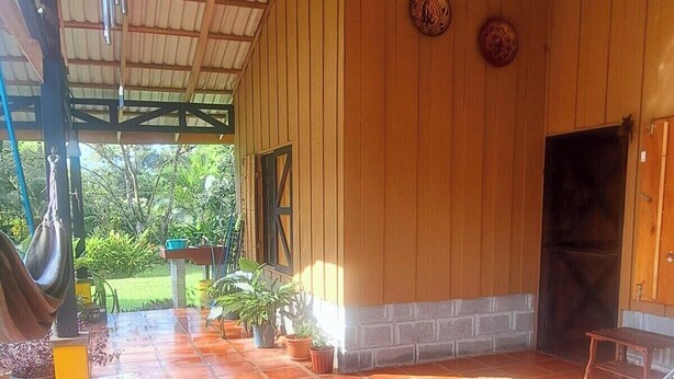 Un patio couvert avec des carreaux de terre cuite, un ventilateur de plafond et une vue sur la verdure environnante.