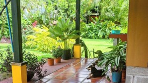 Un patio couvert avec un sol carrelé, des plantes en pot et des meubles d’extérieur.