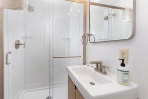 Une salle de bain moderne avec une douche à parois de verre, un lavabo blanc doté d’un distributeur de savon et un miroir au-dessus du lavabo.