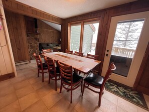 Un coin repas avec une table et des chaises en bois, un mur en pierre et une vue sur une terrasse enneigée, visible à travers une porte vitrée.