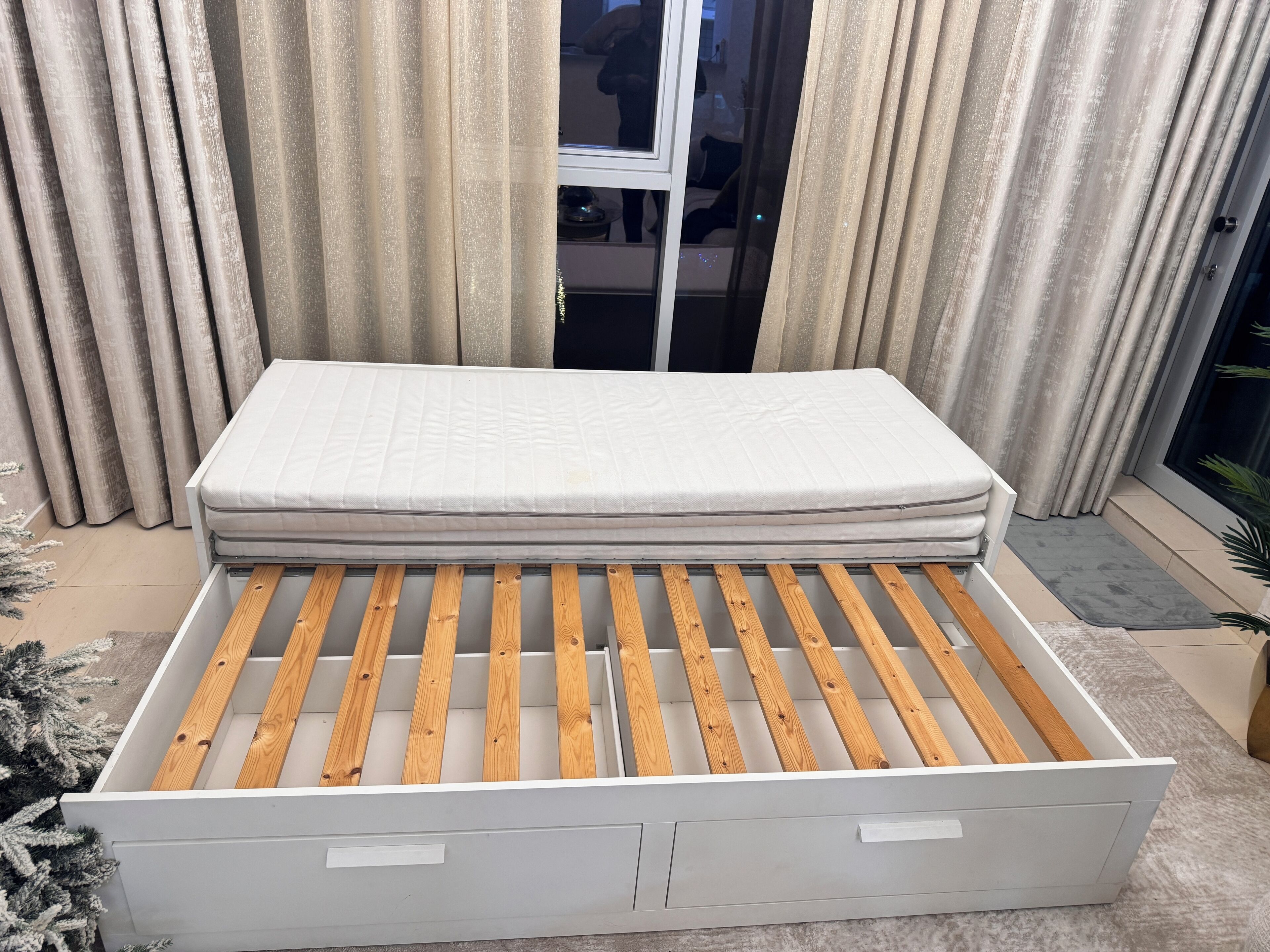 A bed with a wooden frame and a mattress, set against a backdrop of curtains and a window.