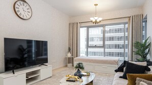 Ein modernes Wohnzimmer mit großem Flachbildfernseher, einer Couch, einem Couchtisch und einem Fenster mit Vorhängen.
