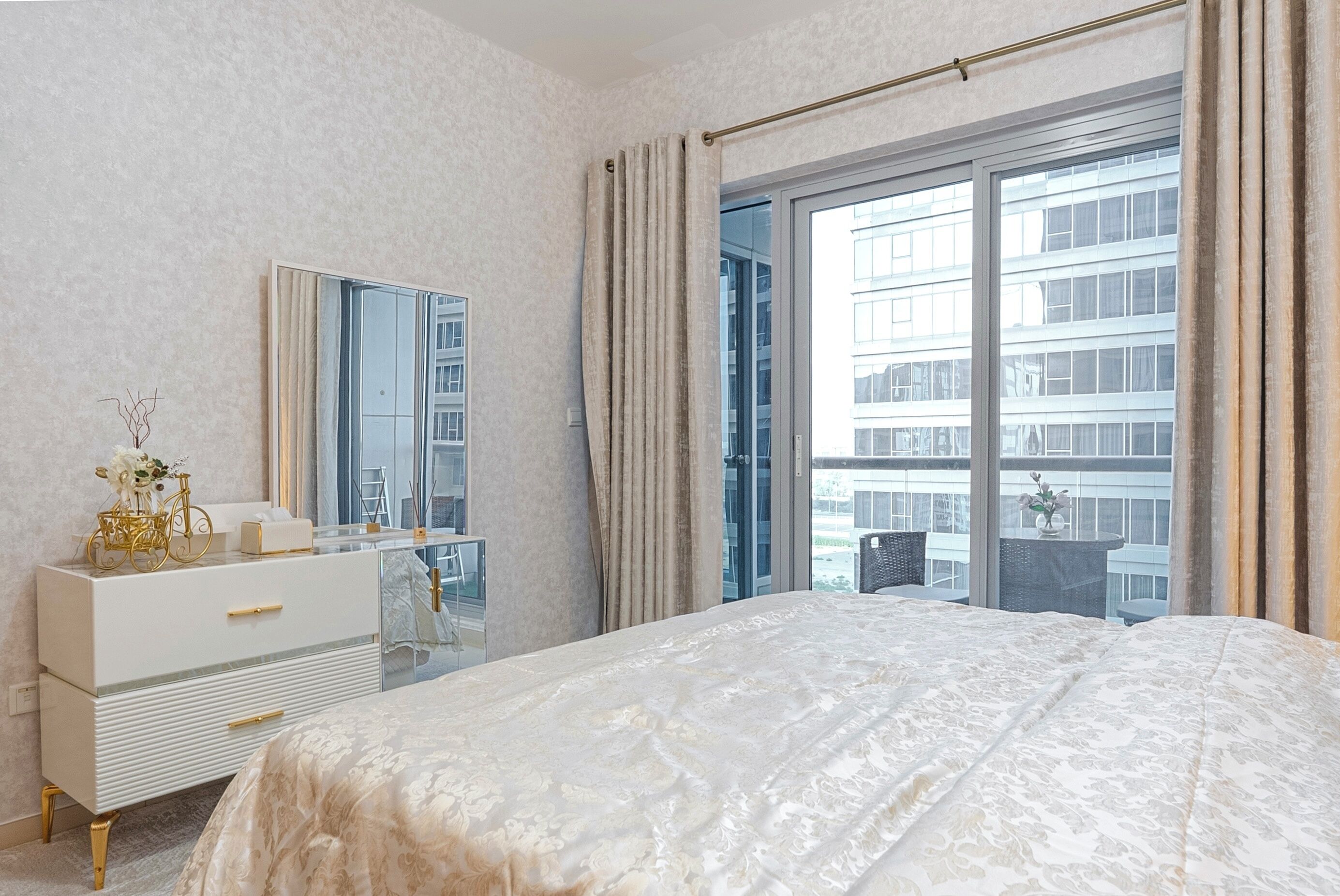 A bedroom with a large bed, a dresser, a mirror, and a window with curtains.