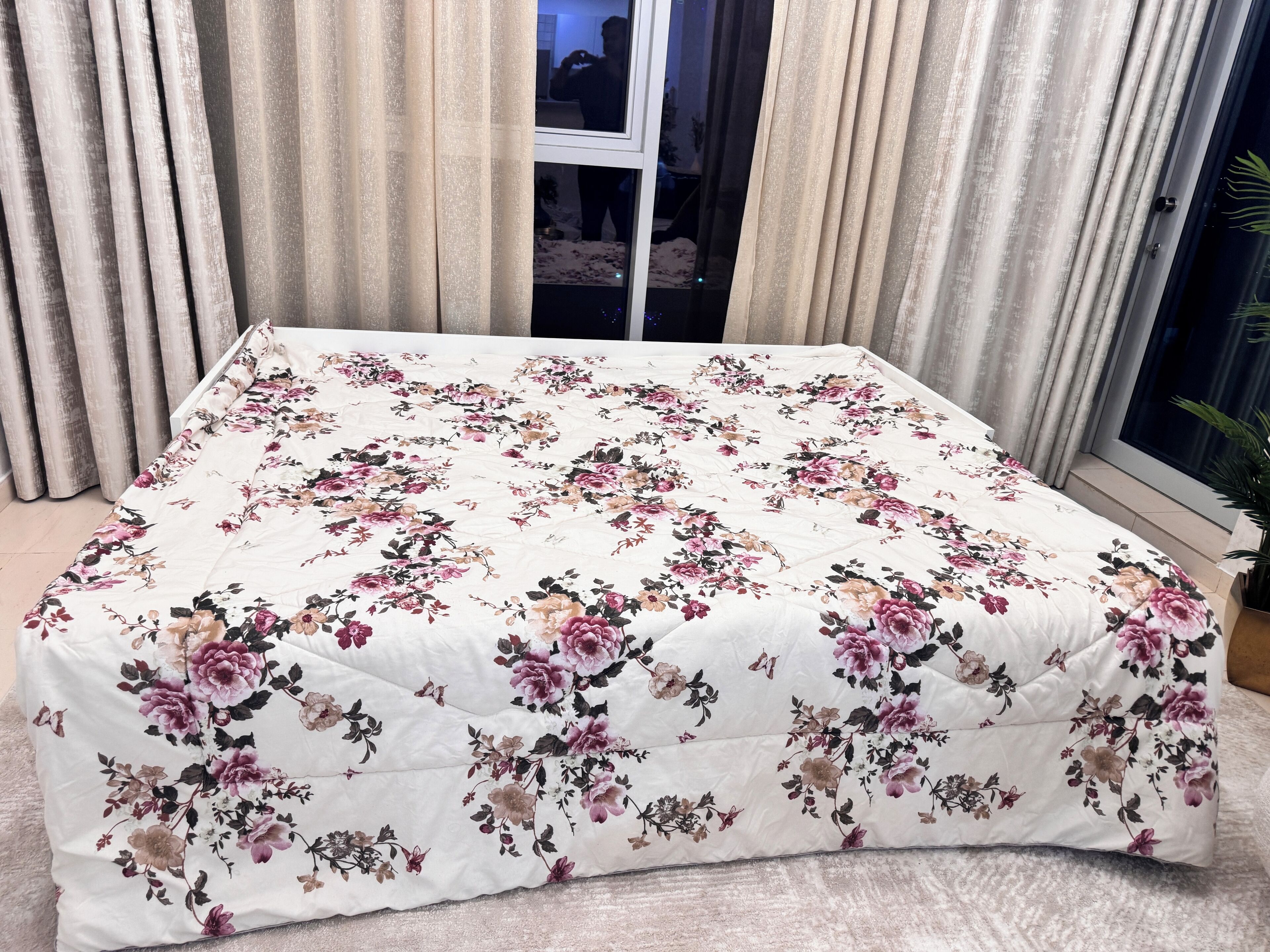 Ein Bett mit blumigem Überwurf in einem Zimmer mit Vorhängen und einem Fenster.