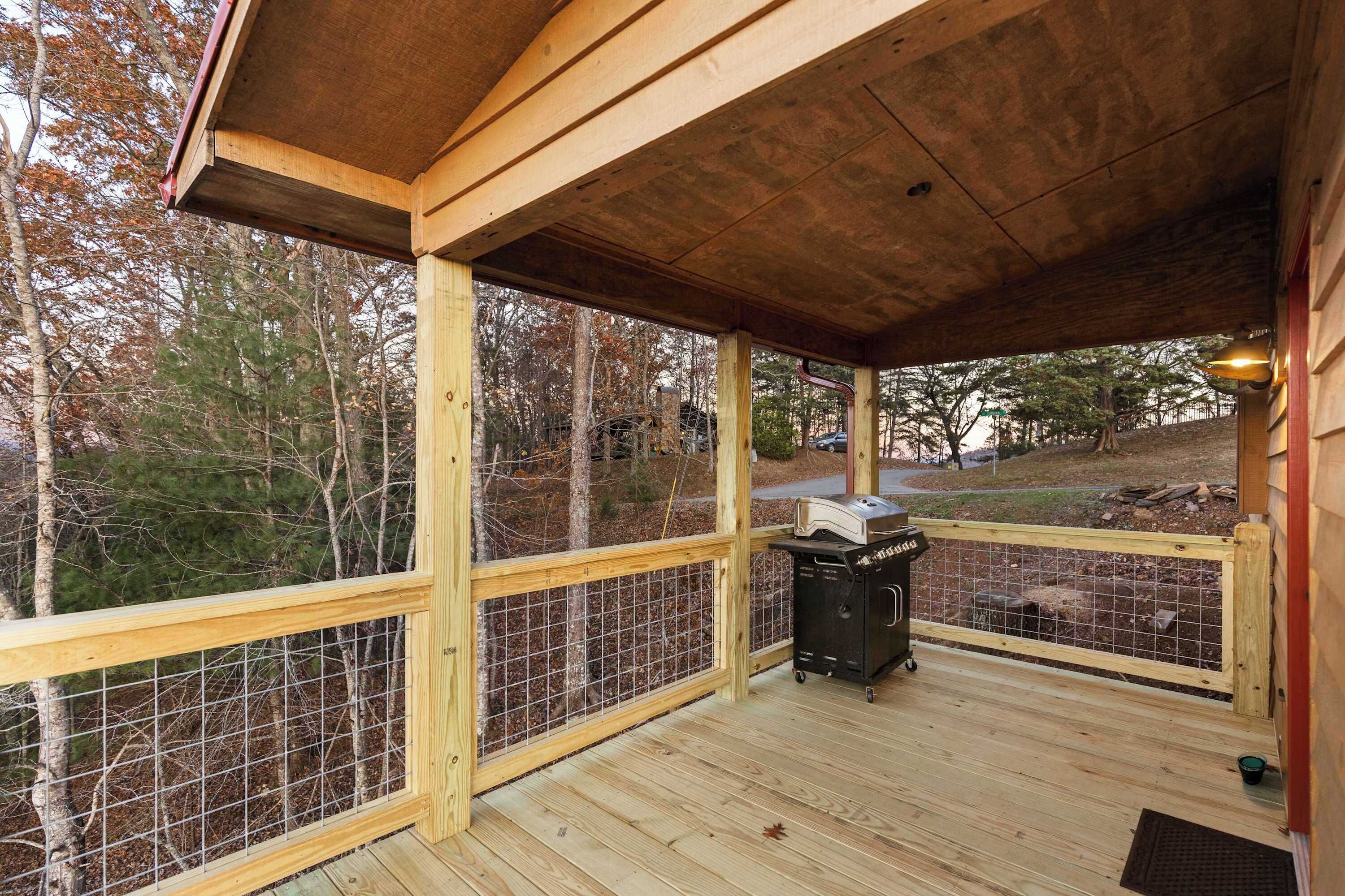 A covered wooden deck with a grill and a fenced area.