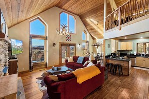Ein großzügiger Wohnbereich mit einem roten Sofa, Holzboden und großen Fenstern mit Blick ins Freie.