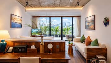 A modern hotel room with a wooden desk, a sofa, a TV, and a balcony with a city view.