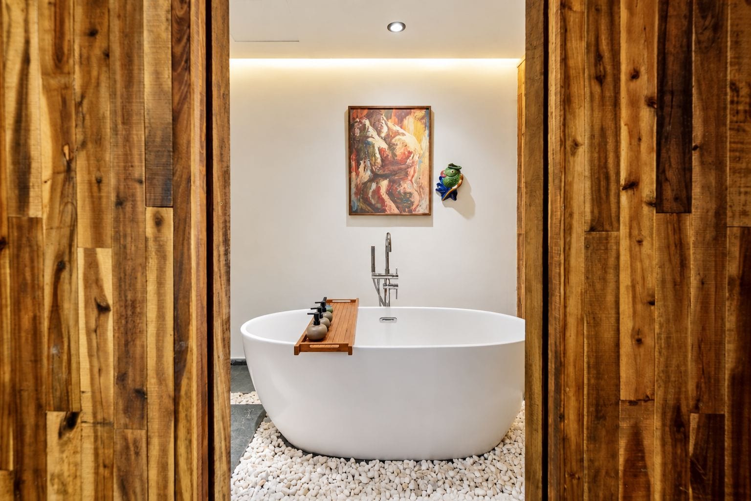 Un baño moderno con una bañera independiente, suelo de madera y un cuadro decorativo en la pared.