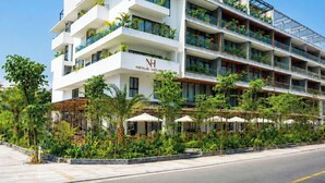 A multi-story hotel with balconies, outdoor seating, and a clear sky. - Nexus House Retreat Xuan Thuy (Ho Chi Minh City)