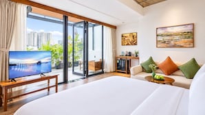 Ein modernes Hotelzimmer mit einem großen Bett, einem Fernseher, einer Couch, einem Couchtisch und Blick auf die Stadt durch die Glastüren.