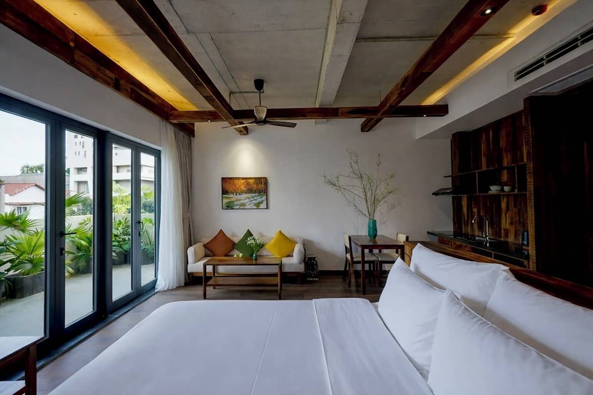 A bedroom with a large bed, a sofa, a dining table, and a view of the outdoors.
