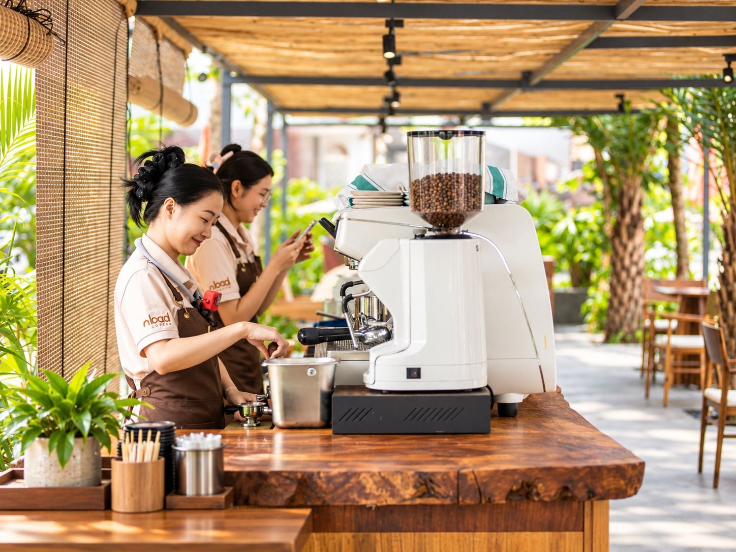 A coffee shop with a coffee machine and a grinder, and two baristas working.