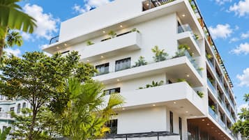 Een hotel met meerdere verdiepingen, balkons, grote ramen en weelderige begroeiing.