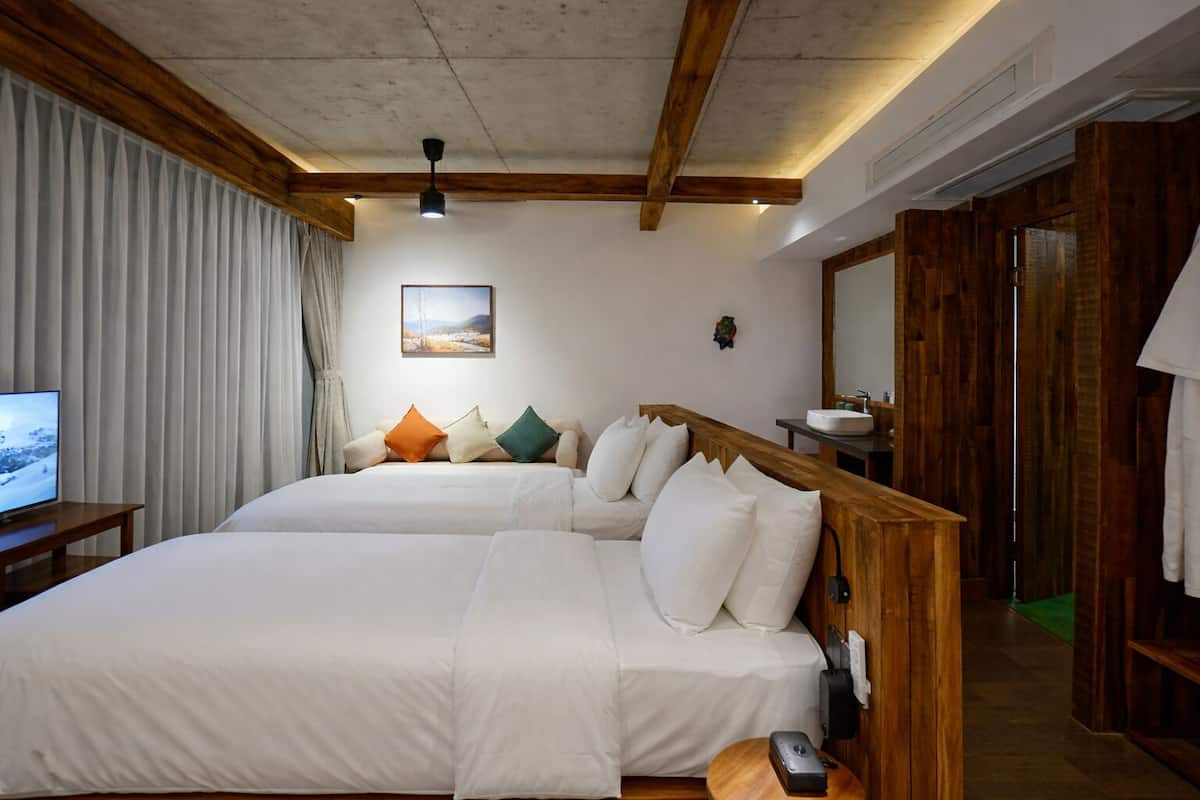 A hotel room with a large bed, a television on a side table, a wooden headboard, and a painting on the wall.