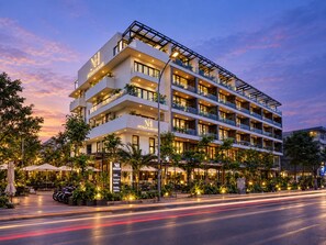 Een meerlaags hotel met balkons, buiten zitplaatsen en een goed verlichte ingang.