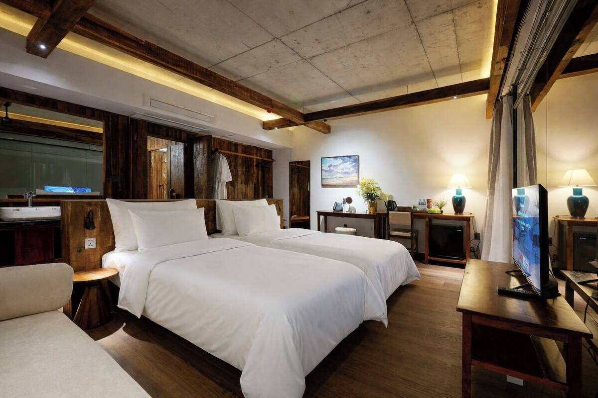 A hotel room with two beds, a desk, a TV, and a bathroom with a sink and mirror.