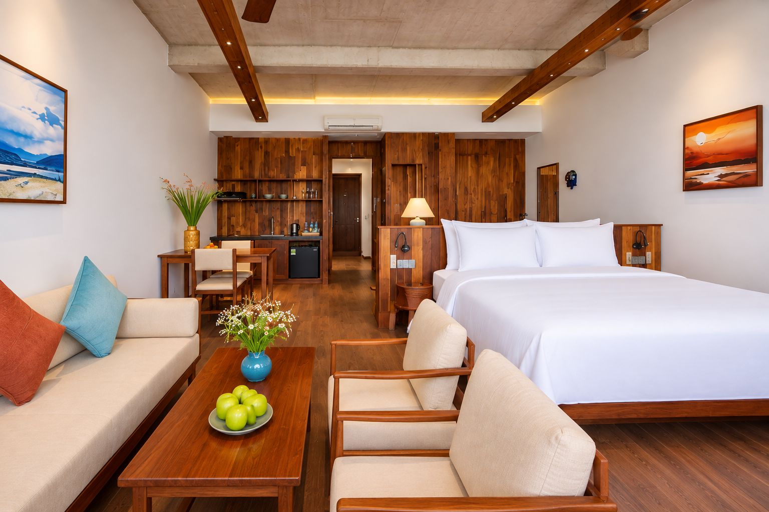 A hotel room with a bed, a sofa, a dining table with apples, and a kitchen area.