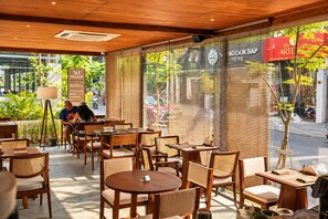 Um café com móveis de madeira e grandes janelas, com um letreiro para 'NOKUBAP' e 'the ARTIST'.