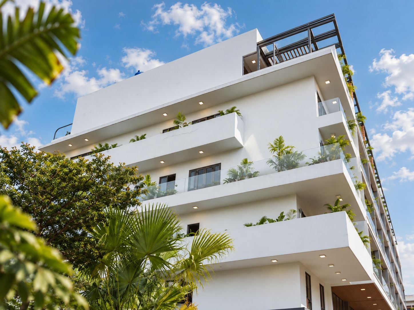 A multi-story building with balconies, some with plants, and a clear sky.