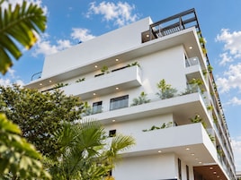 Un edificio de varios pisos con balcones, algunos con plantas, y un cielo despejado.
