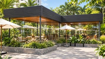 A modern outdoor seating area with tables and chairs under umbrellas, surrounded by lush greenery and a clear sky.