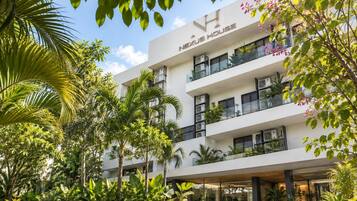 A multi-story hotel with a modern design, featuring balconies with plants, and surrounded by lush greenery.