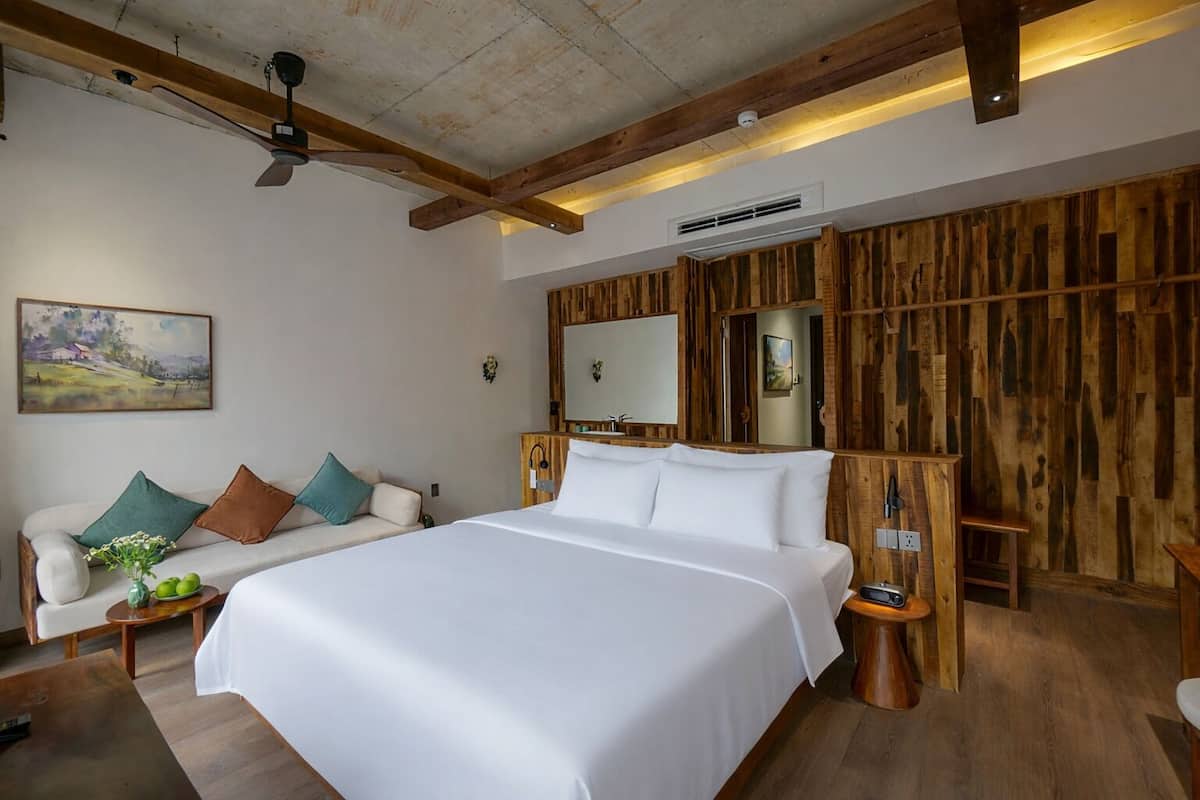 A bedroom with a large bed, a wooden headboard, a ceiling fan, and a painting on the wall.