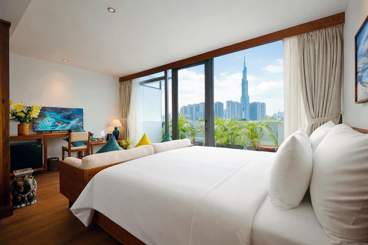 A modern hotel room with a large bed, a desk with a computer, and a view of a city skyline.