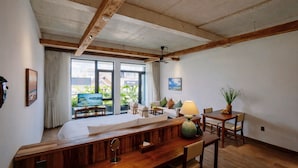 A spacious room with a wooden dining table, a sofa, and a TV. There is a large window with curtains, and a ceiling fan is visible. - Nexus House Retreat Xuan Thuy (Ho Chi Minh City)