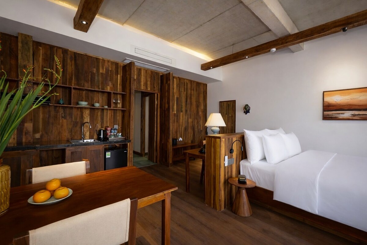 A compact hotel room with a wooden interior, a kitchenette, a dining area, and a bed.
